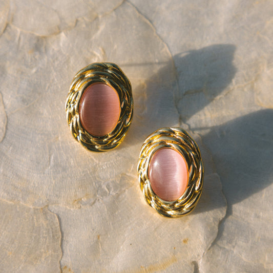 Pair of gold earrings with pink stones on a textured stone surface
