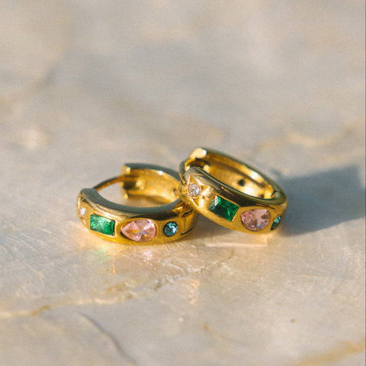 Gold hoop earrings with gemstones on a textured surface
