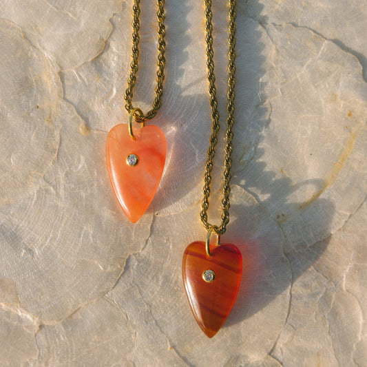 Two heart-shaped pendants on gold chains against a stone background
