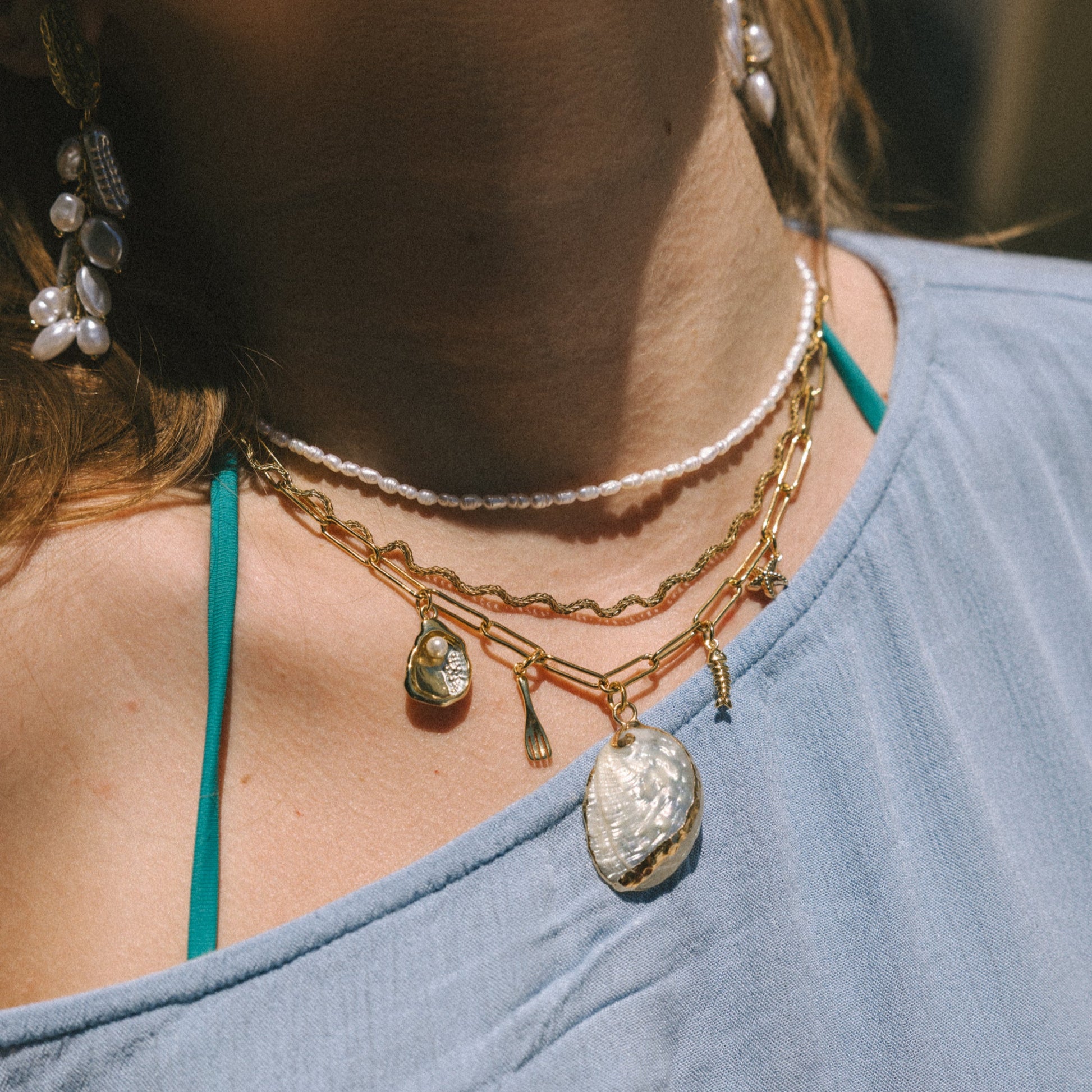 Close-up of a person wearing multiple necklaces with pendants on a blurred background