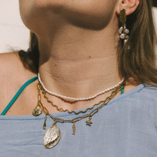 Close-up of a woman wearing layered necklaces and earrings with a blurred background