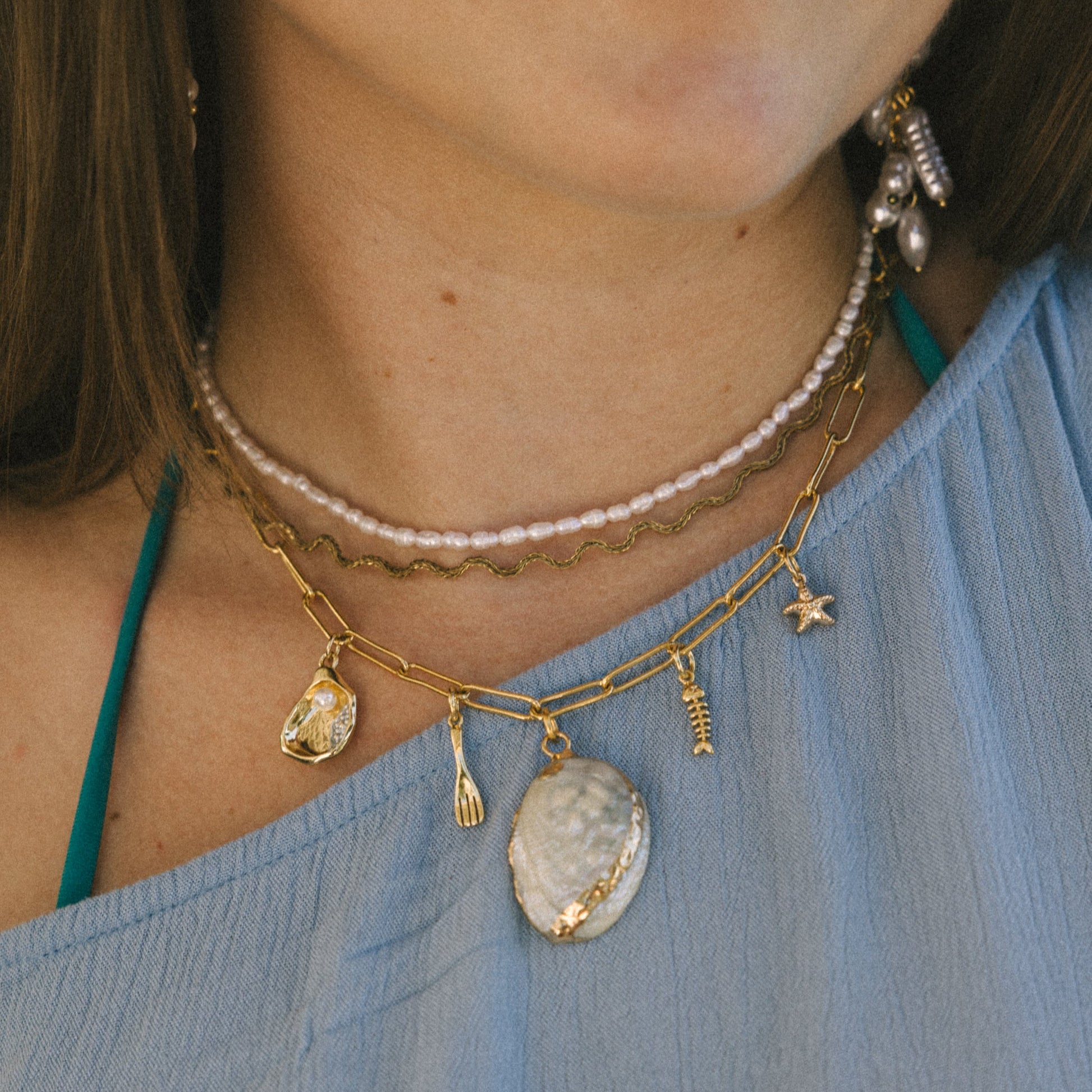 Close-up of a person wearing multiple necklaces with pendants on a blue top.