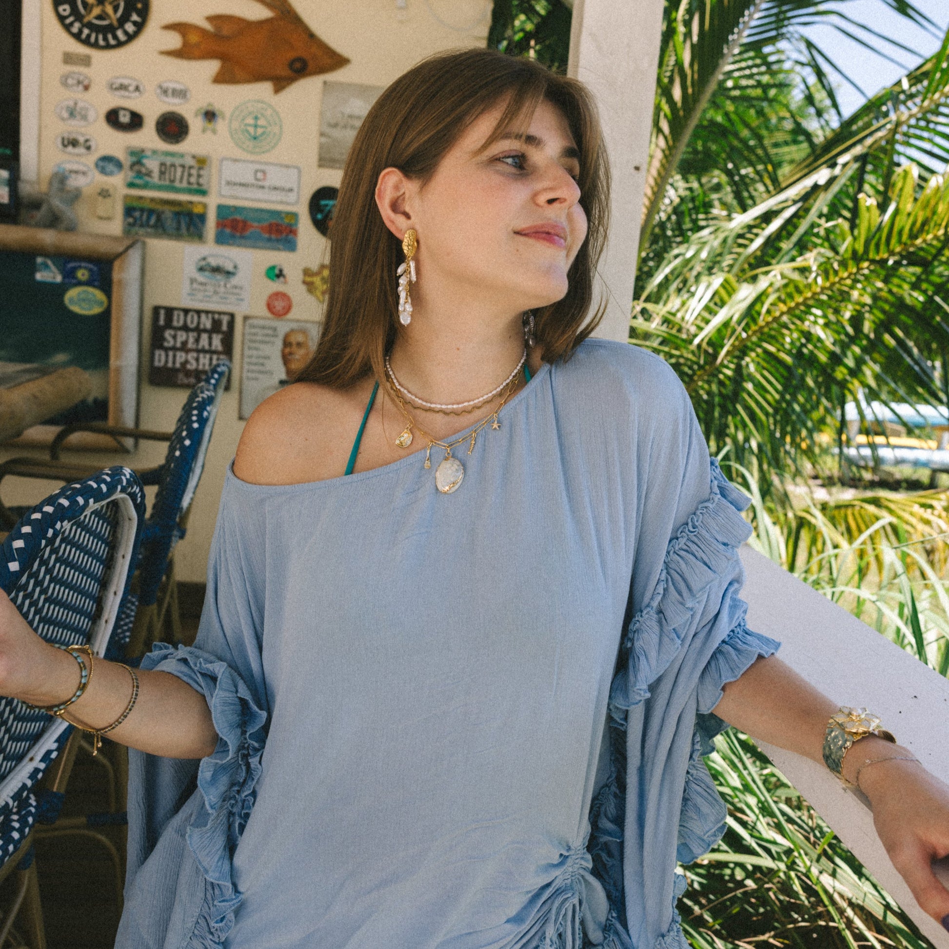 Woman in a blue dress standing outdoors with palm trees and a casual setting.