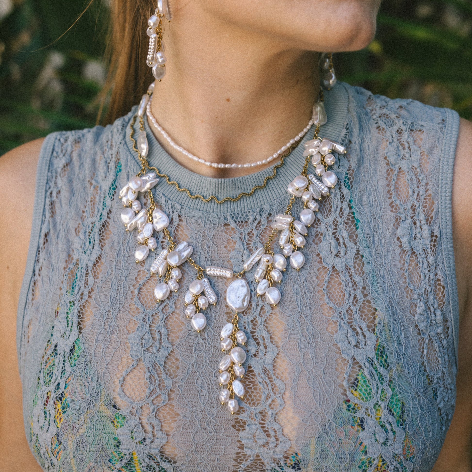 Woman wearing a detailed necklace with a textured sleeveless top outdoors.