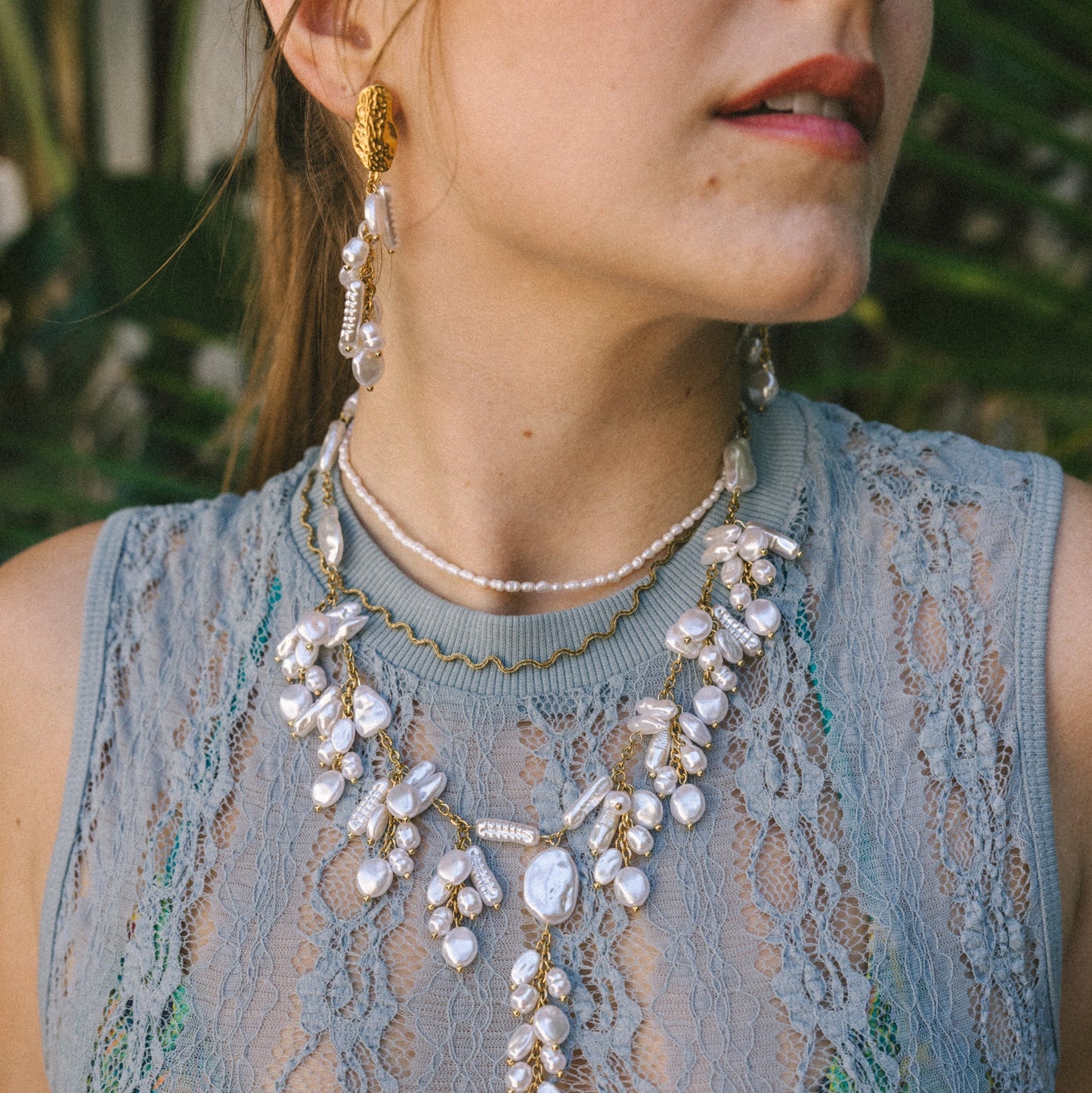 Woman wearing a detailed necklace with a textured sleeveless top outdoors.