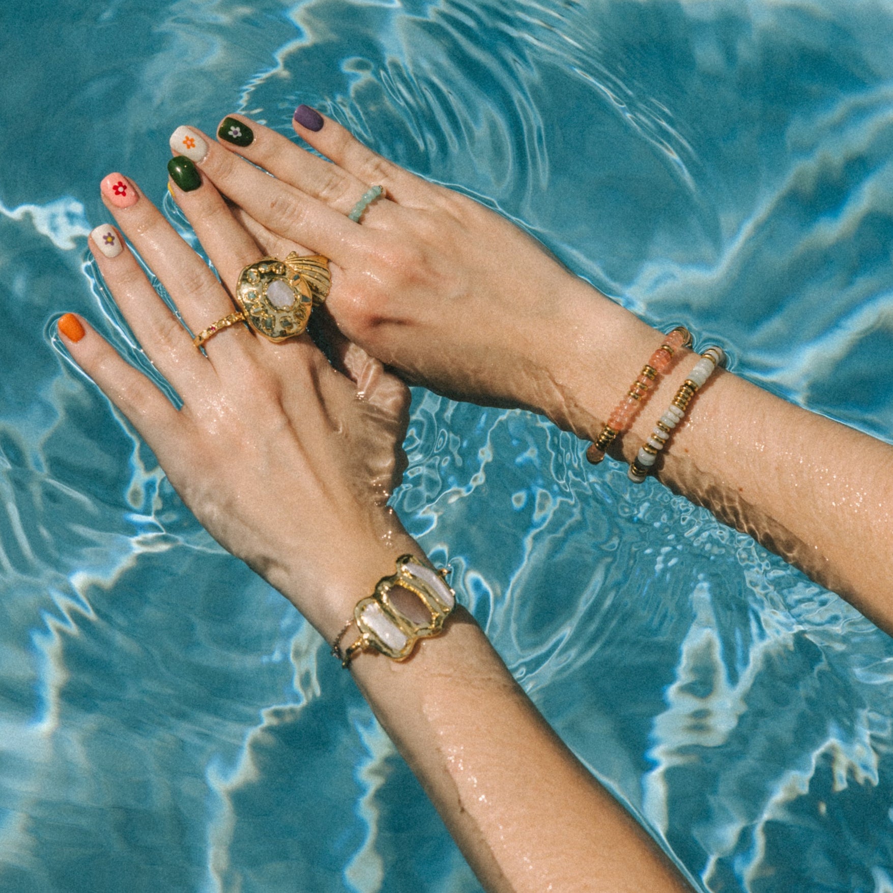 Close-up of hands with rings and bracelets over blue water
