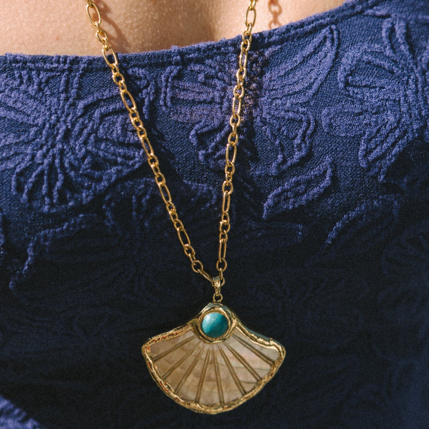 Necklace with a pendant featuring a turquoise stone on a blue textured fabric background