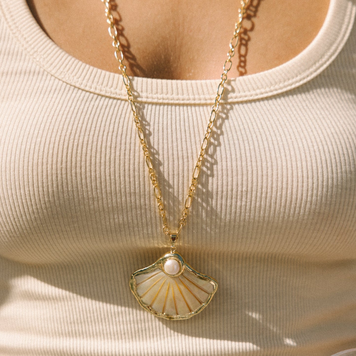 Gold necklace with a shell pendant worn by a person in a beige top.