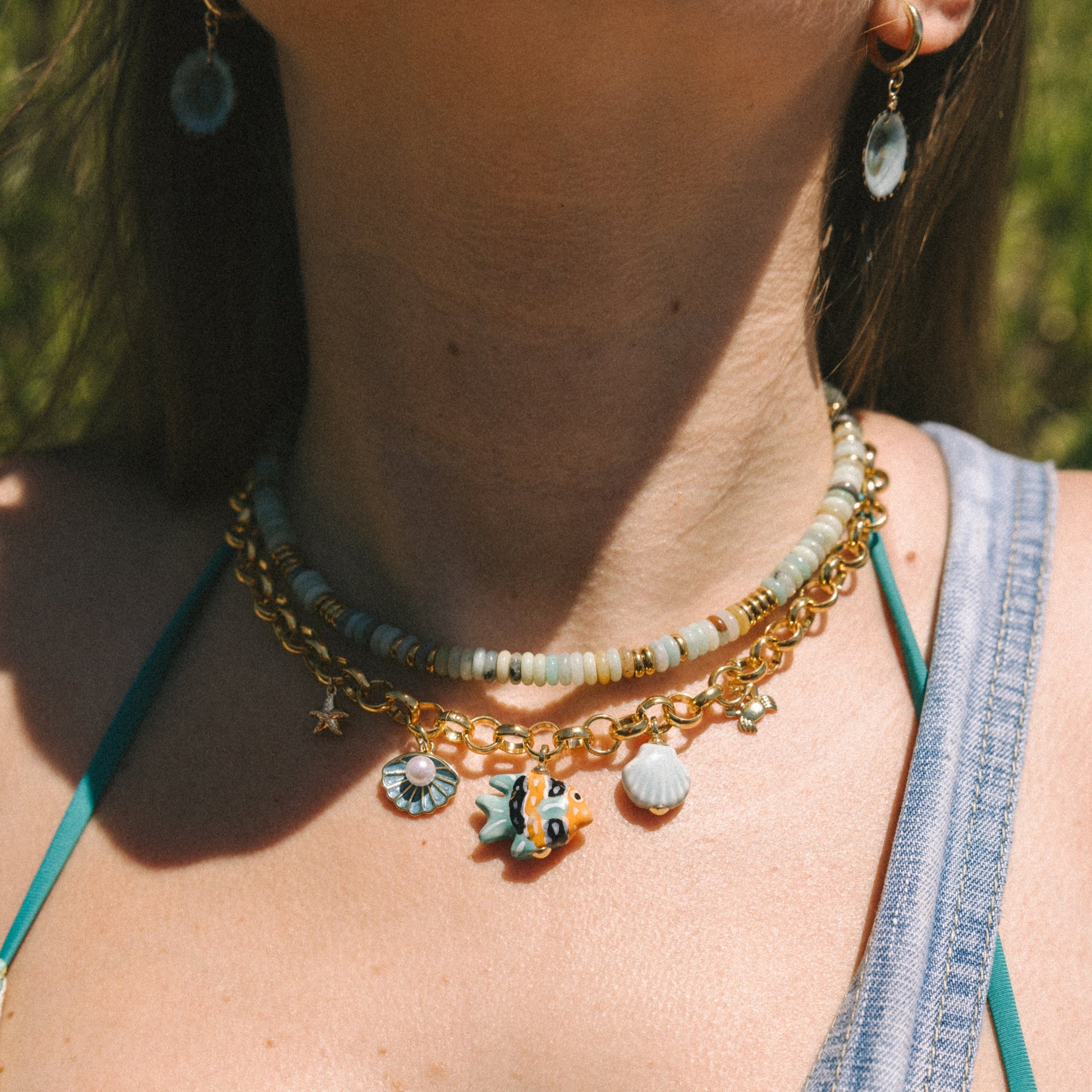 Close-up of a person wearing a gold necklace with charms against a blurred natural background