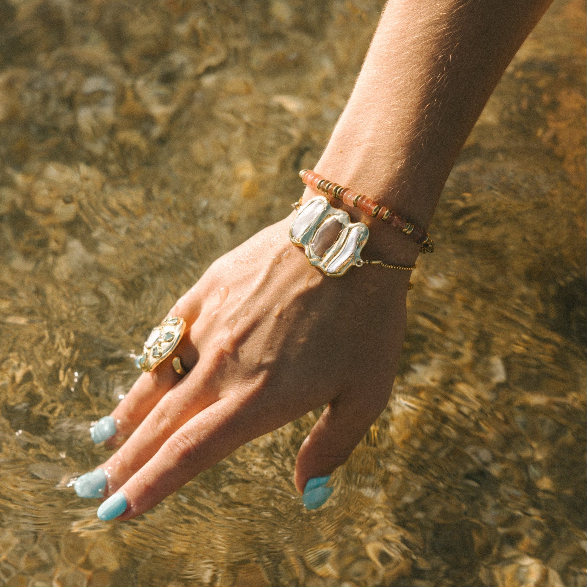 Hand with rings and bracelets touching clear water