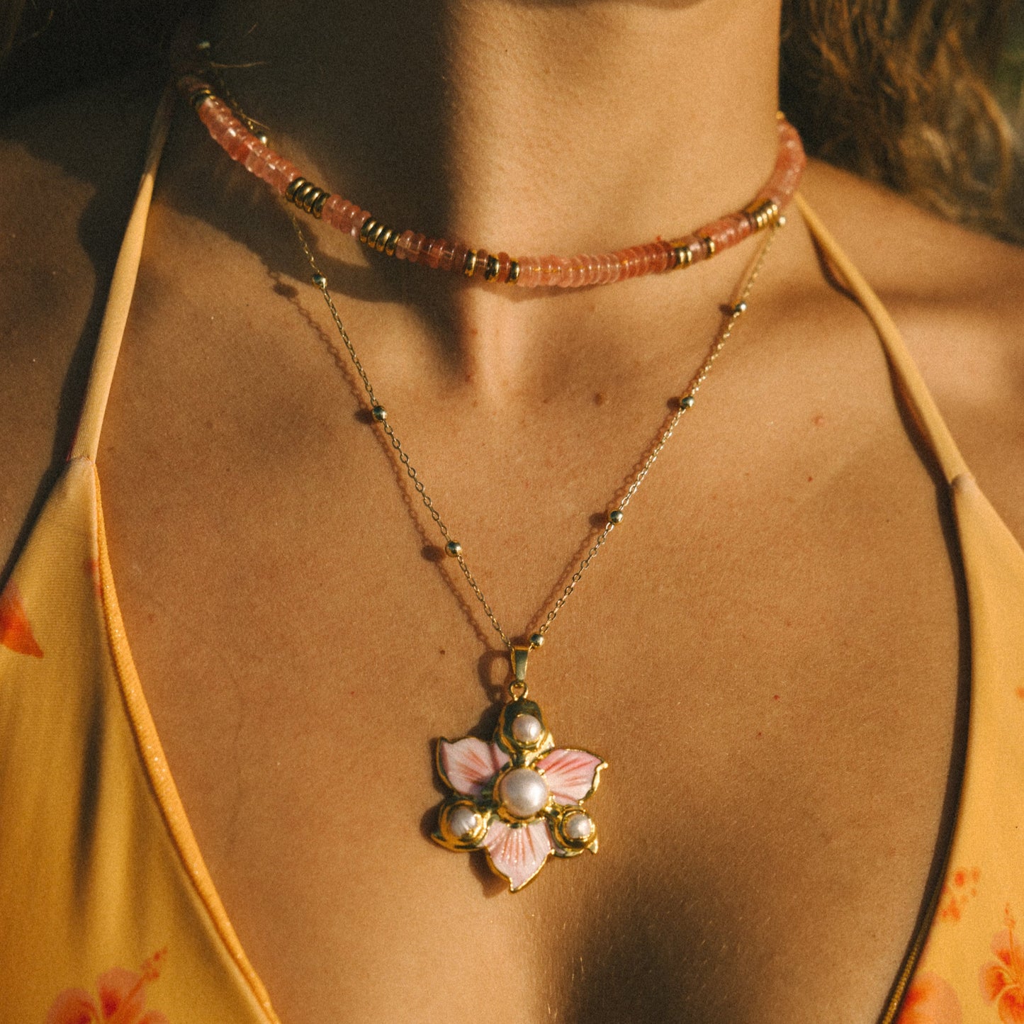 Close-up of a necklace with a floral pendant worn by a person in a yellow top.