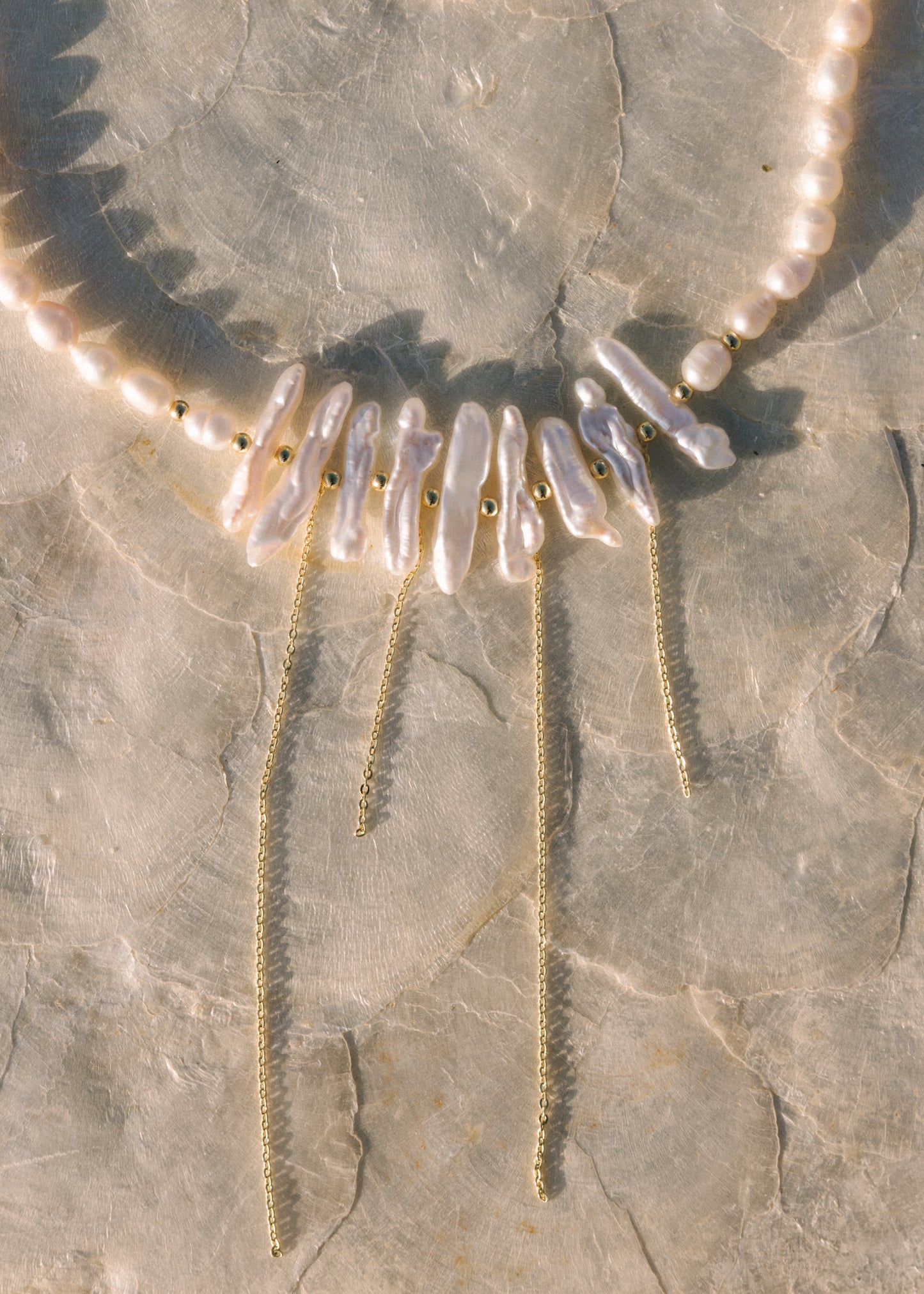 Pearl necklace with gold chain on a stone surface