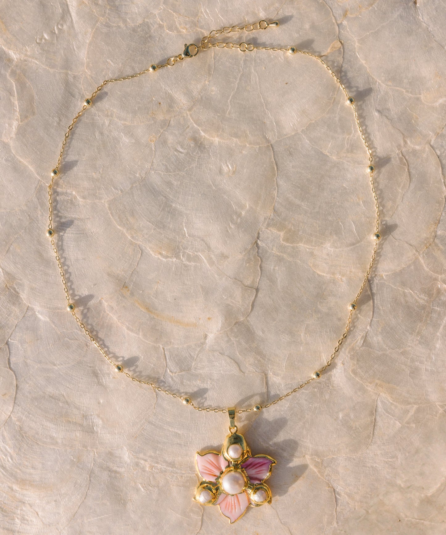Gold necklace with a floral pendant on a stone surface