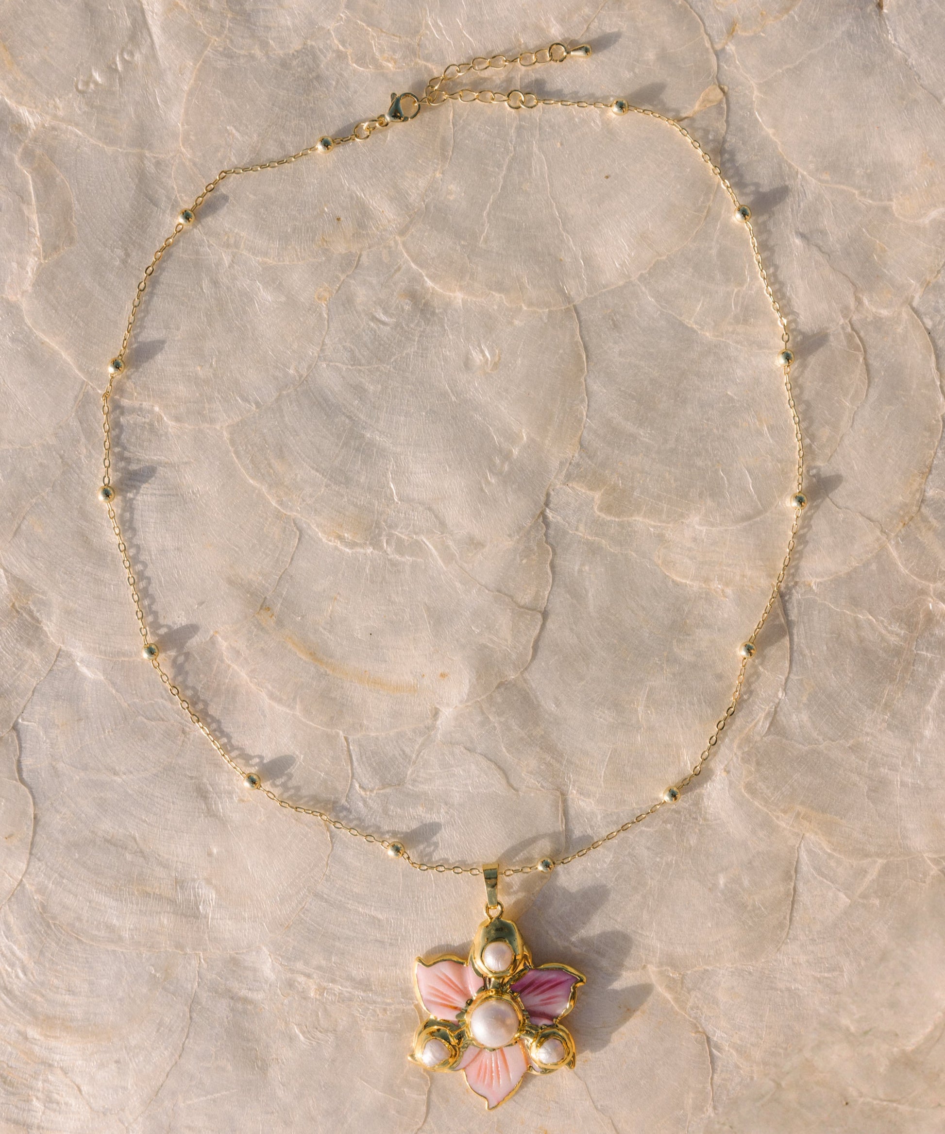 Gold necklace with a floral pendant on a stone surface