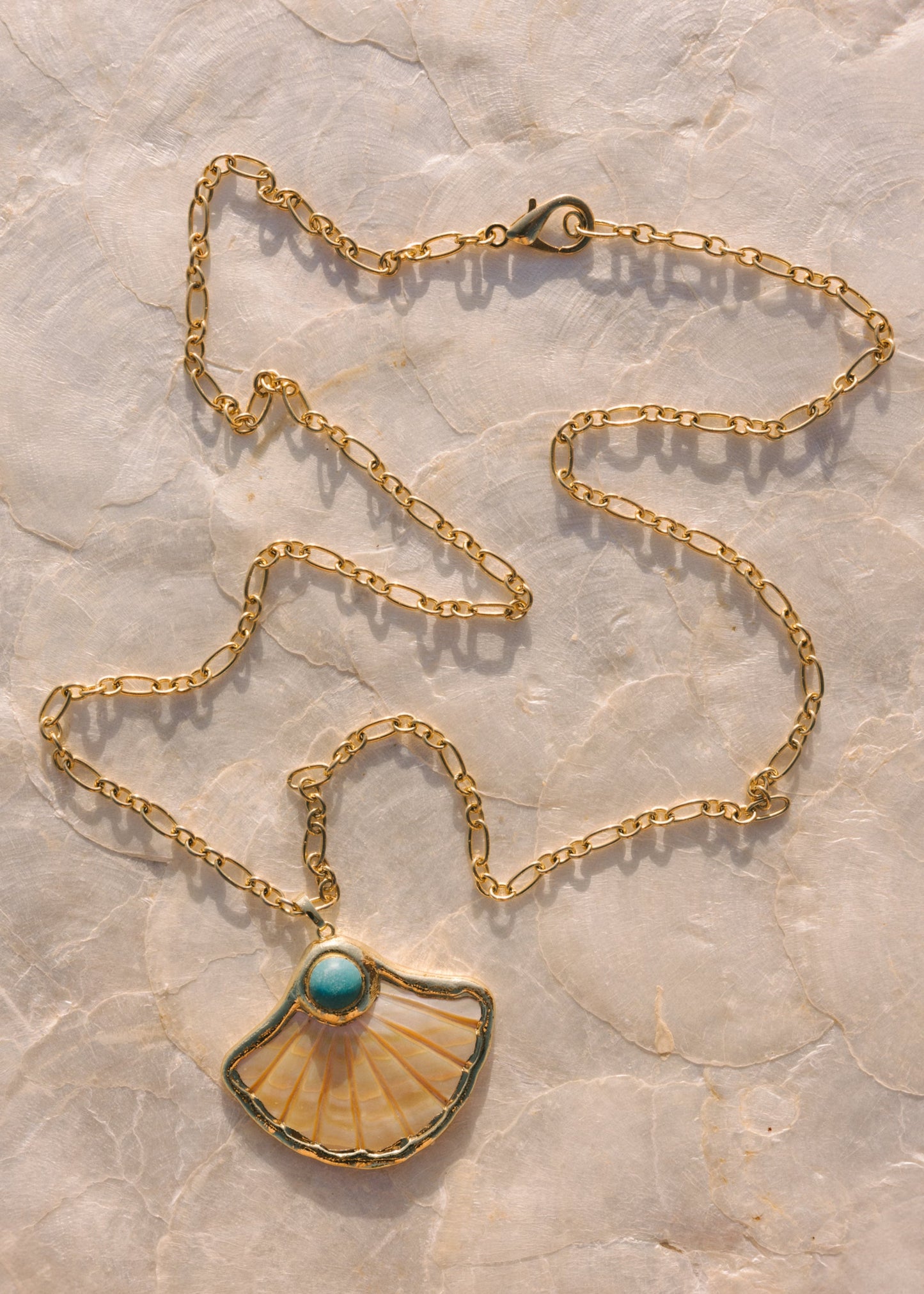 Gold necklace with a shell pendant on a marble surface