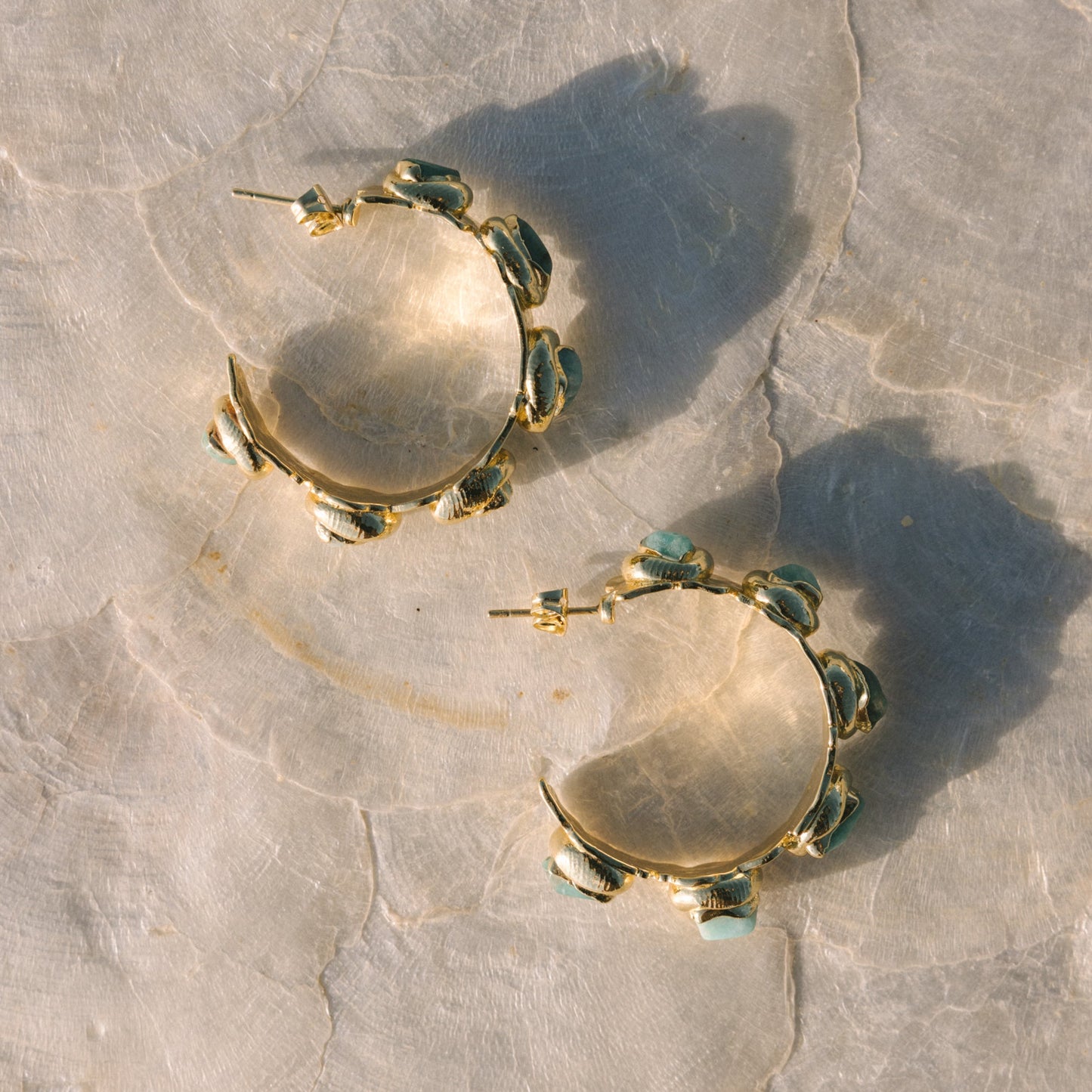 Gold hoop earrings with green accents on a textured stone surface