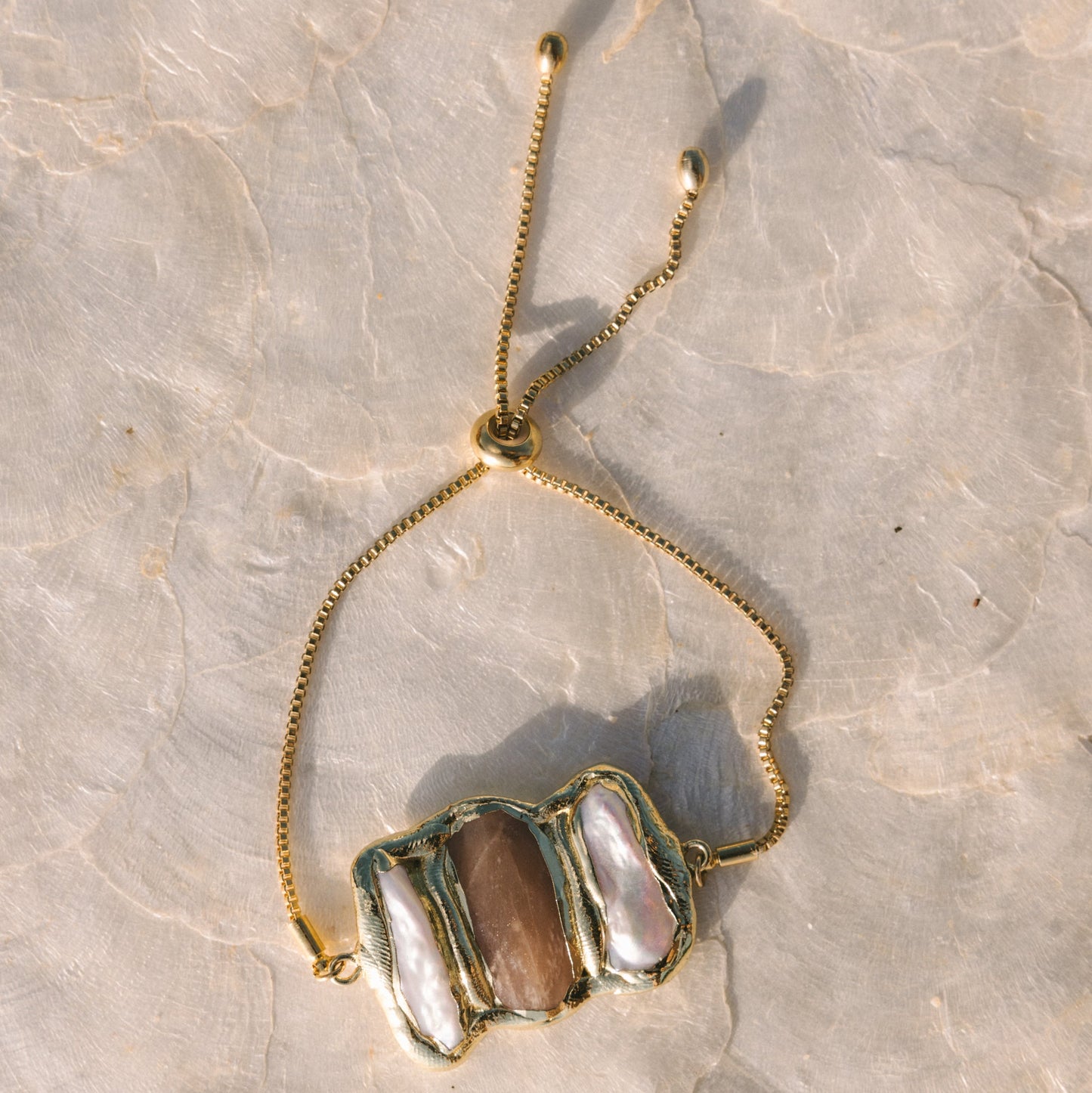 Necklace with a gold chain and stone pendant on a textured surface