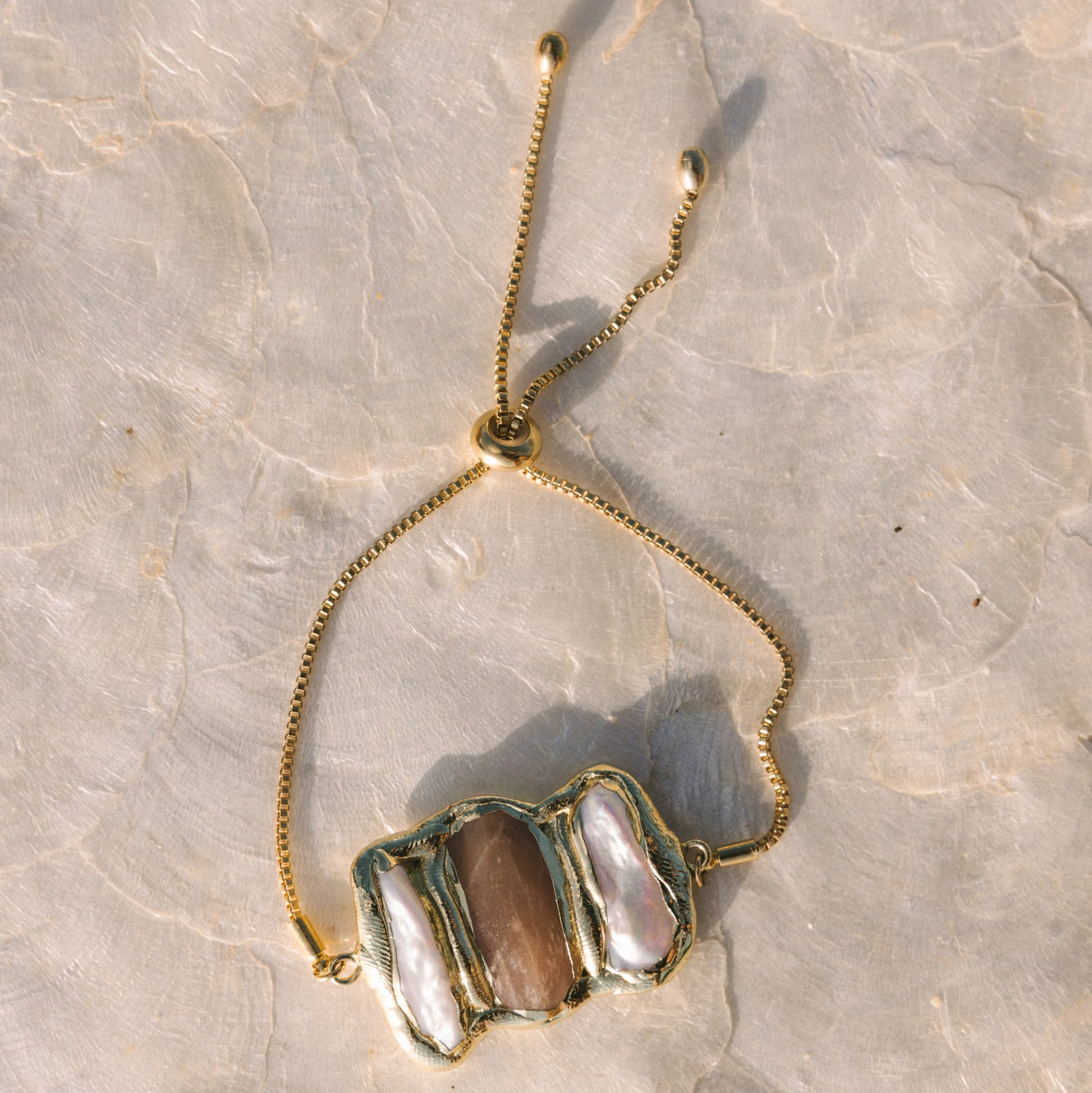 Necklace with a gold chain and stone pendant on a textured surface