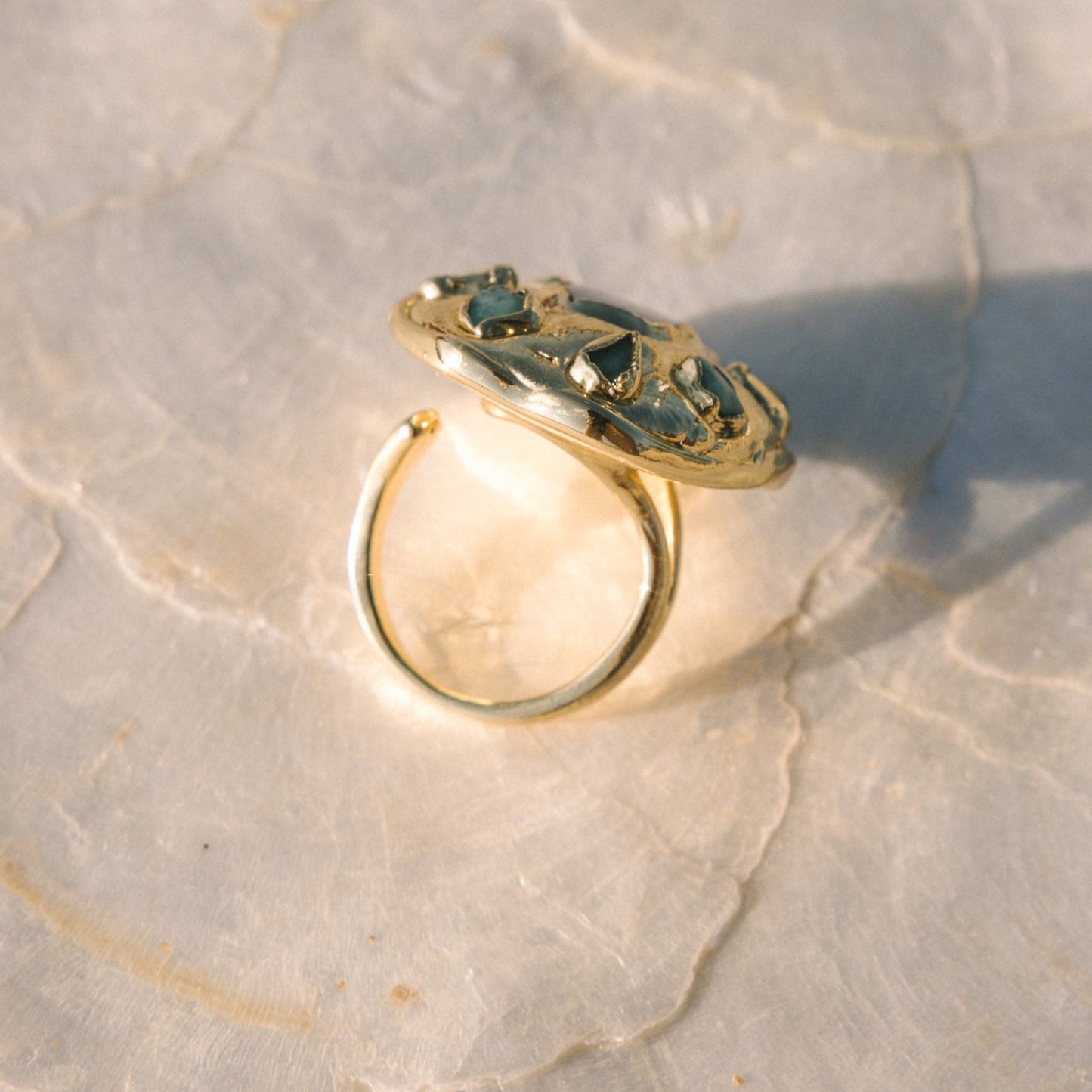Gold ring with green gemstones on a textured stone surface