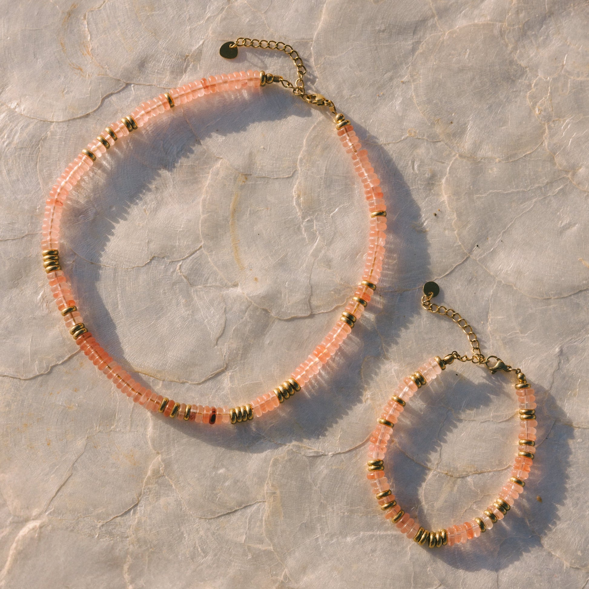 Necklace and bracelet set with pink and gold beads on a stone surface