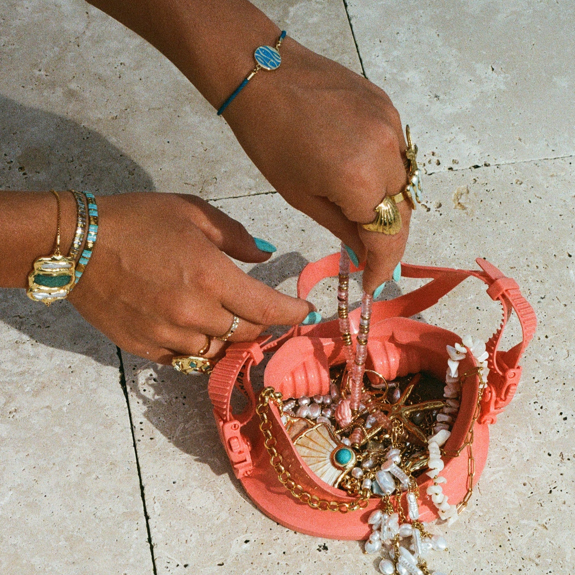 Person organizing jewelry in a pink bag on a light stone pavement.