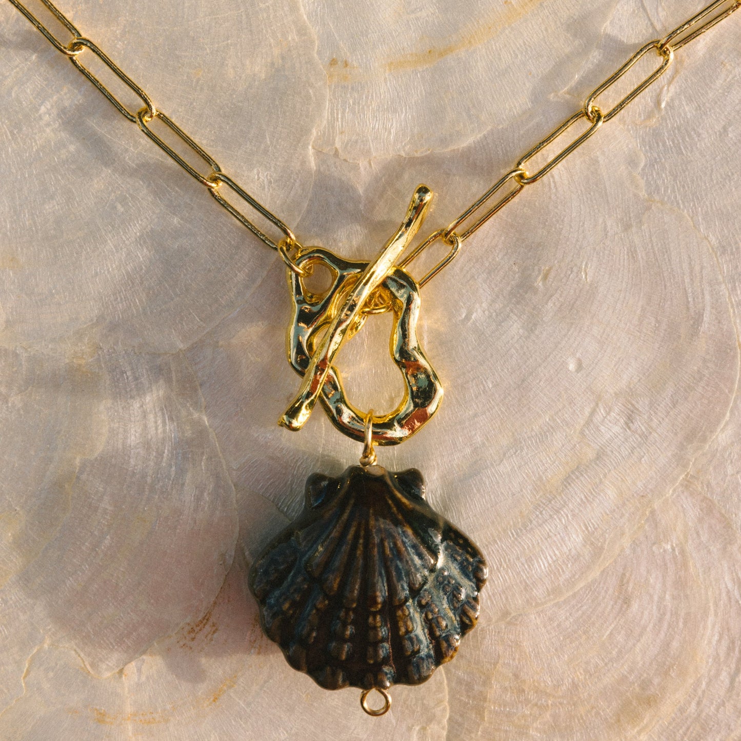 Gold necklace with a black shell pendant on a textured beige background