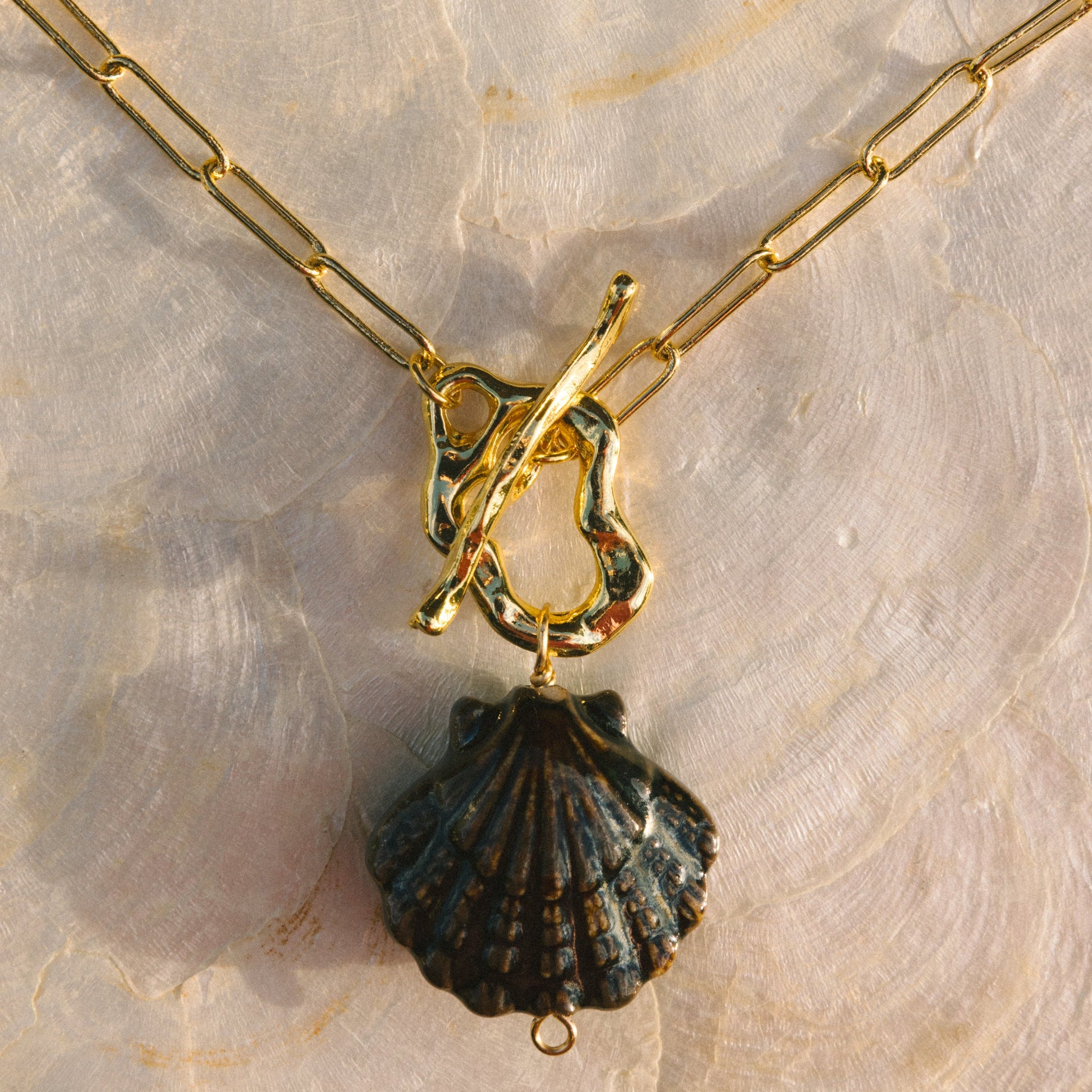 Gold necklace with a black shell pendant on a textured beige background