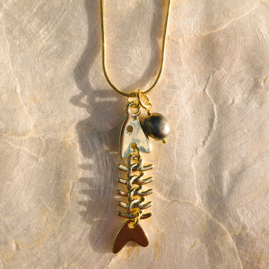 Gold fish bone pendant necklace on a beige stone background
