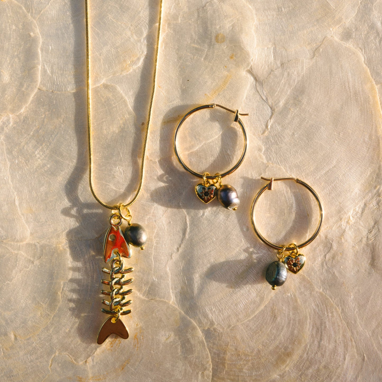 Gold necklace with fish pendant and gold hoop earrings on a stone surface