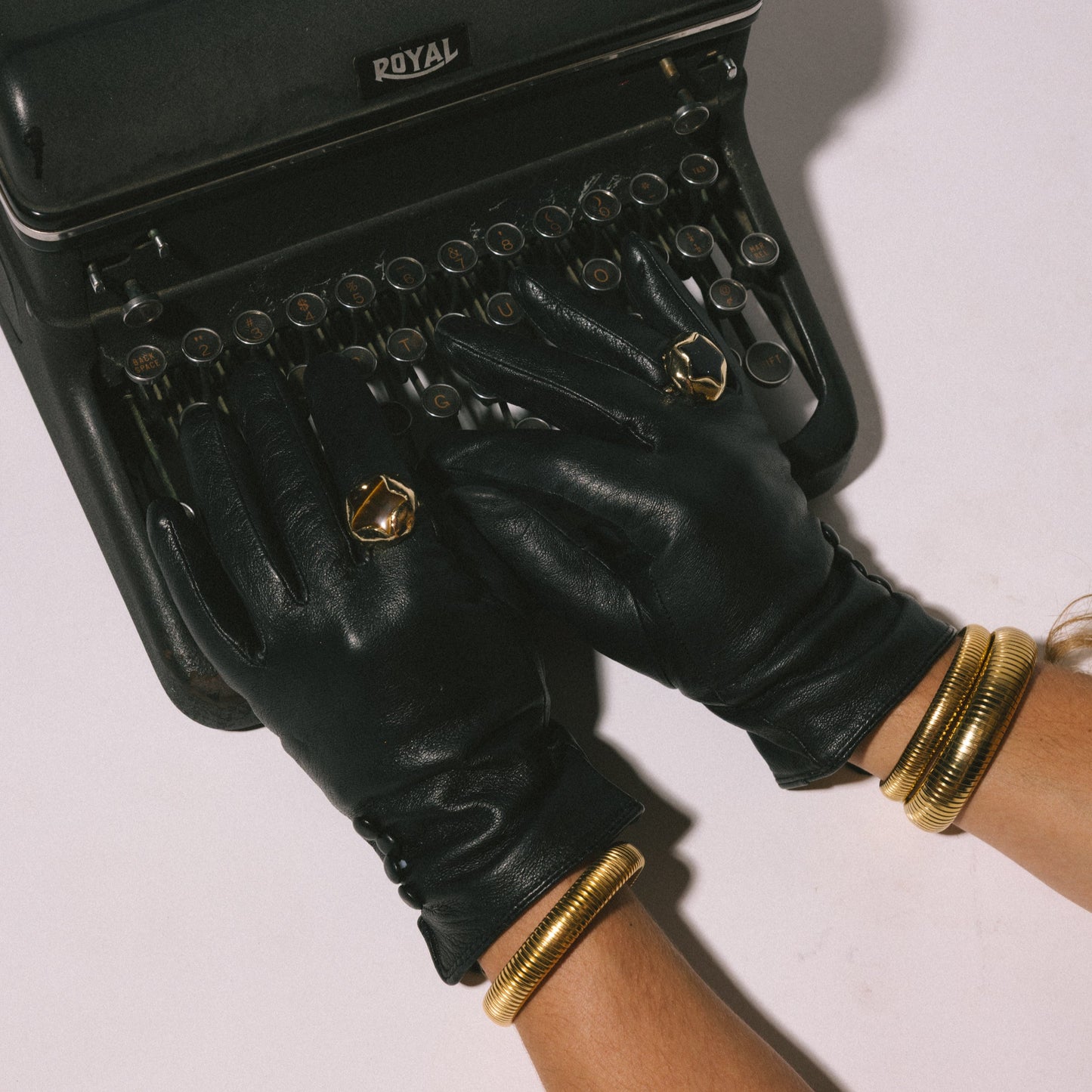 Black leather handbag with gold accents held by a gloved hand on a light background