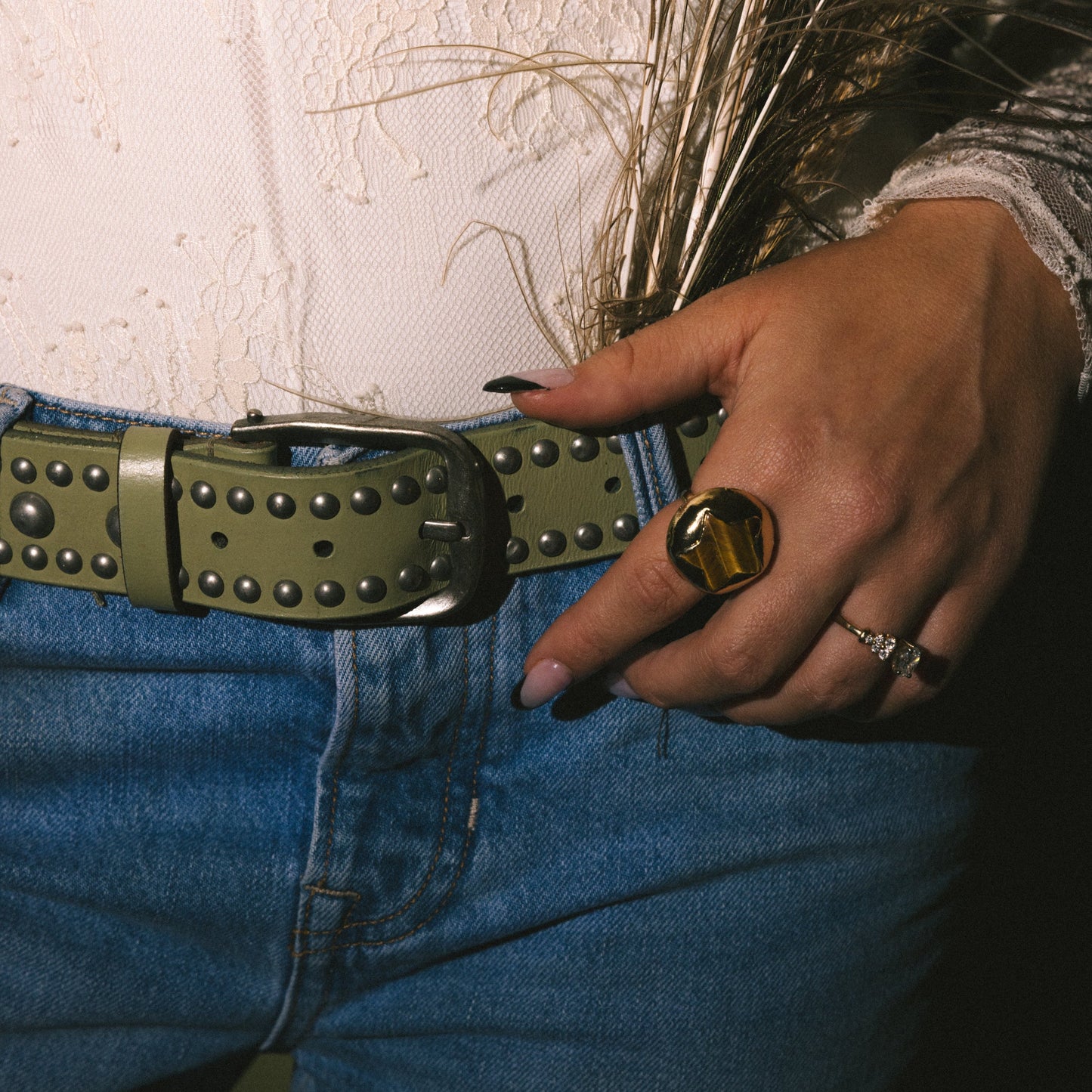 Person wearing blue jeans with a studded belt and holding dried grasses.