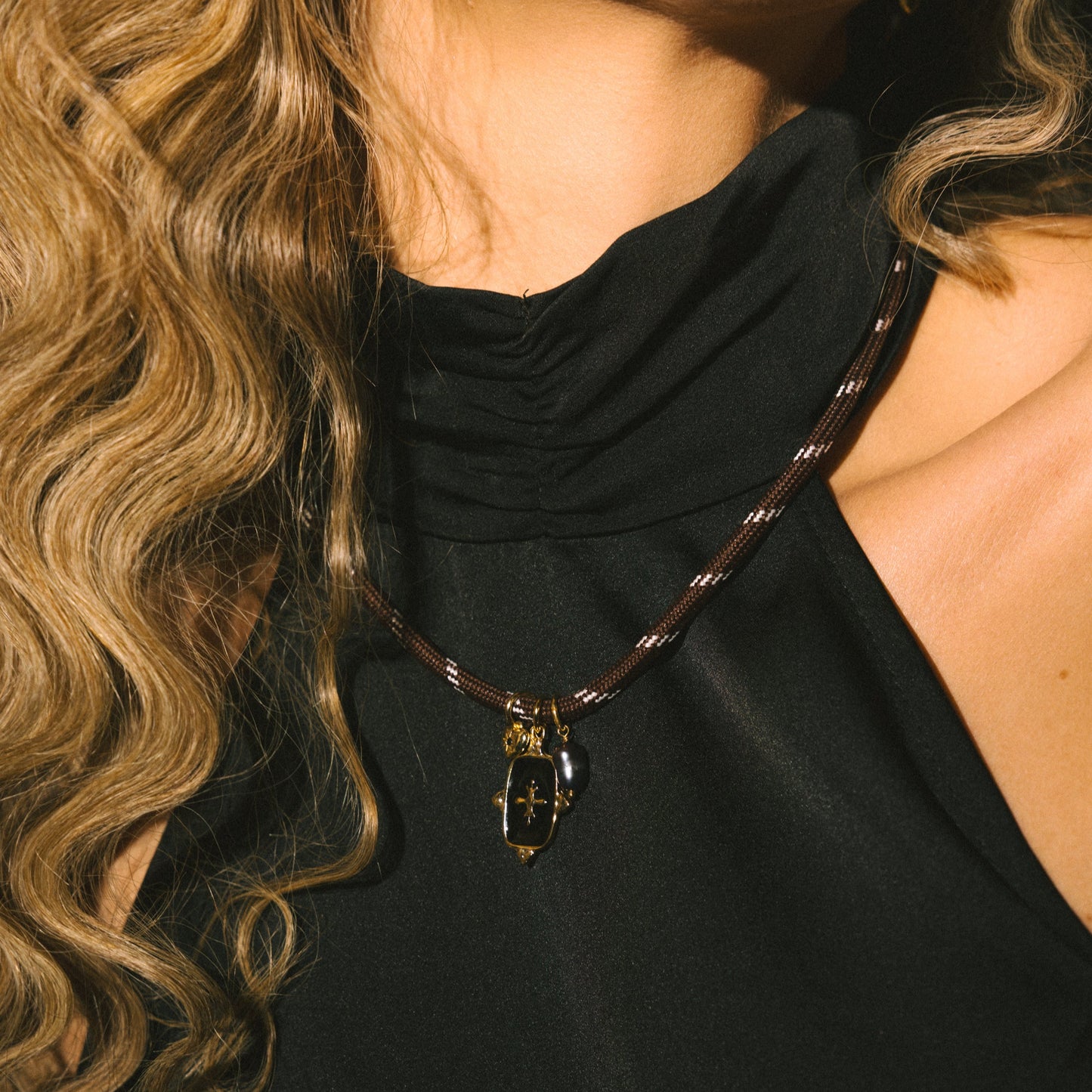 Close-up of a person wearing a black top and a necklace with a pendant.