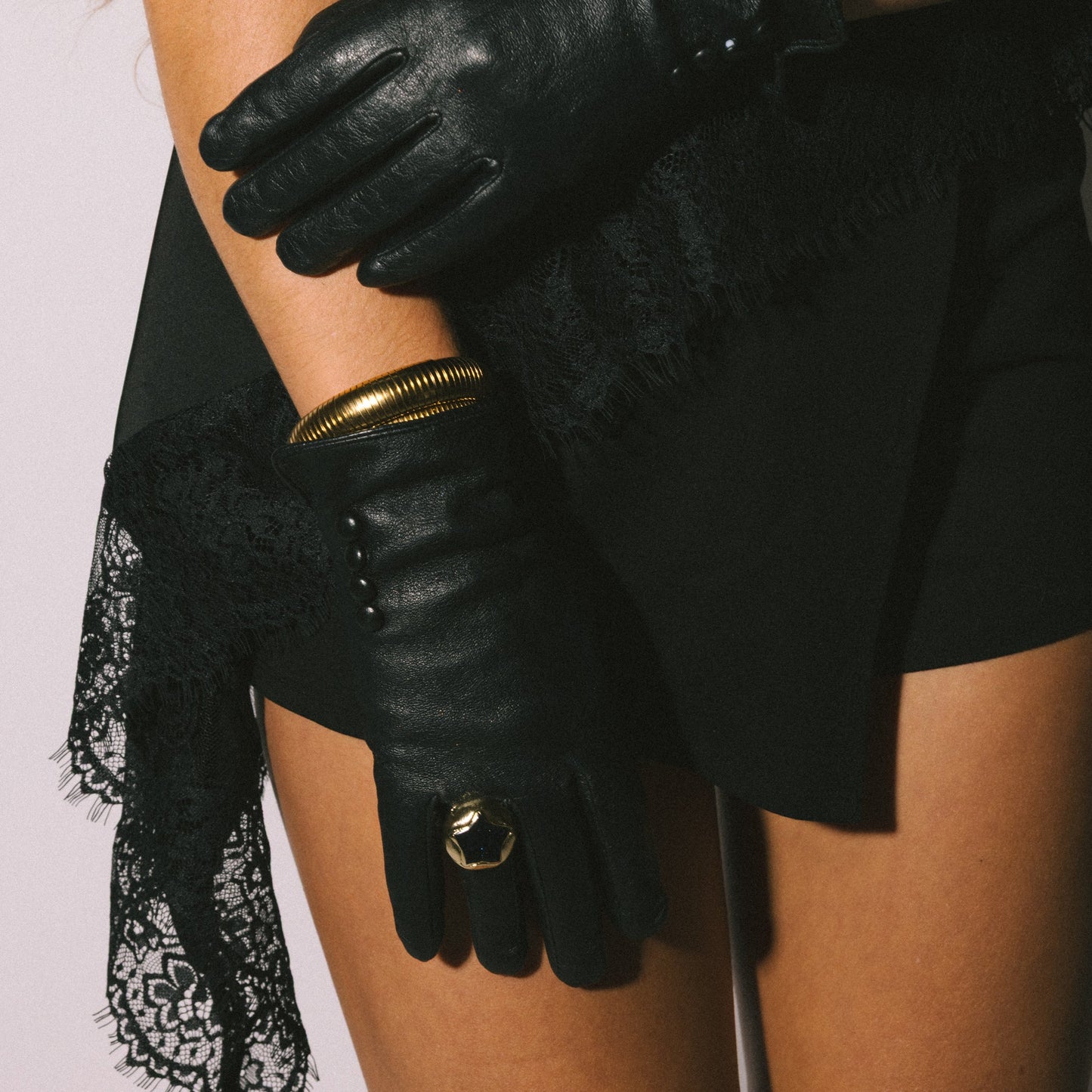 Person wearing black leather gloves with gold accents on a plain background