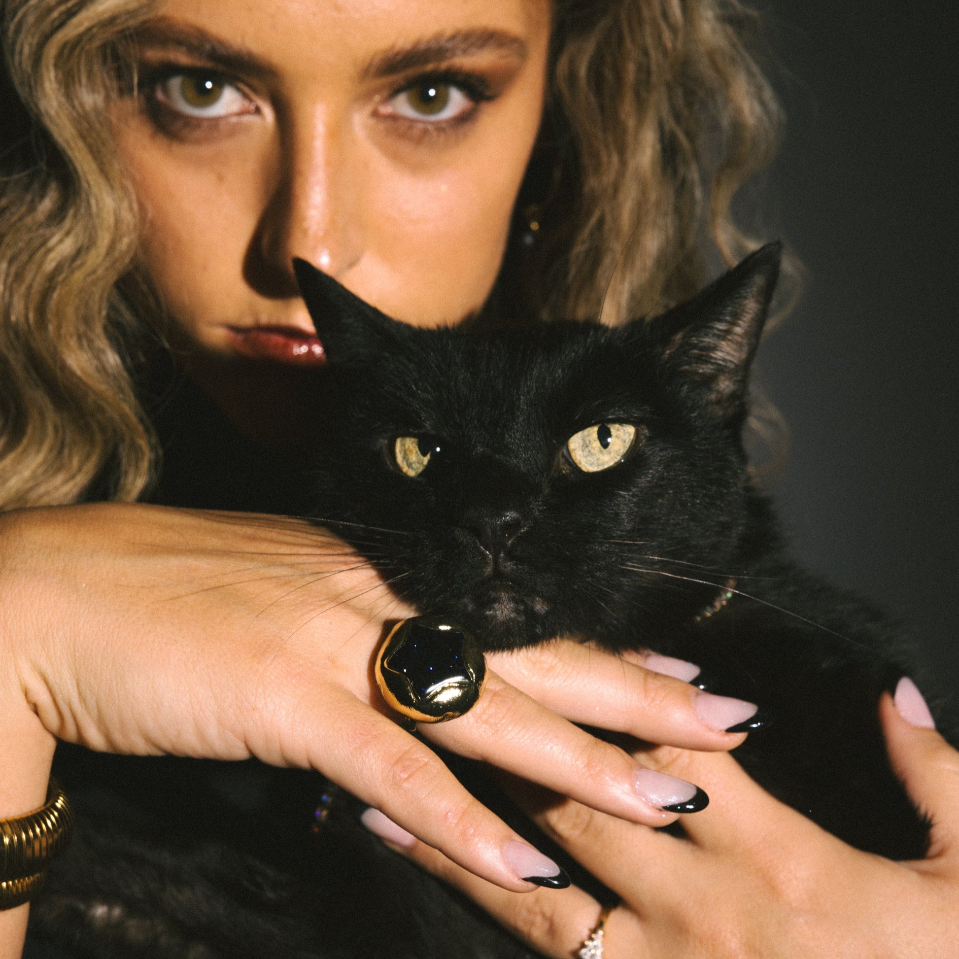 Woman holding a black cat against a dark background
