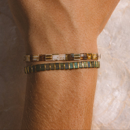 A close-up of a person's hand wearing two beaded bracelets on the wrist set against a light stone background.