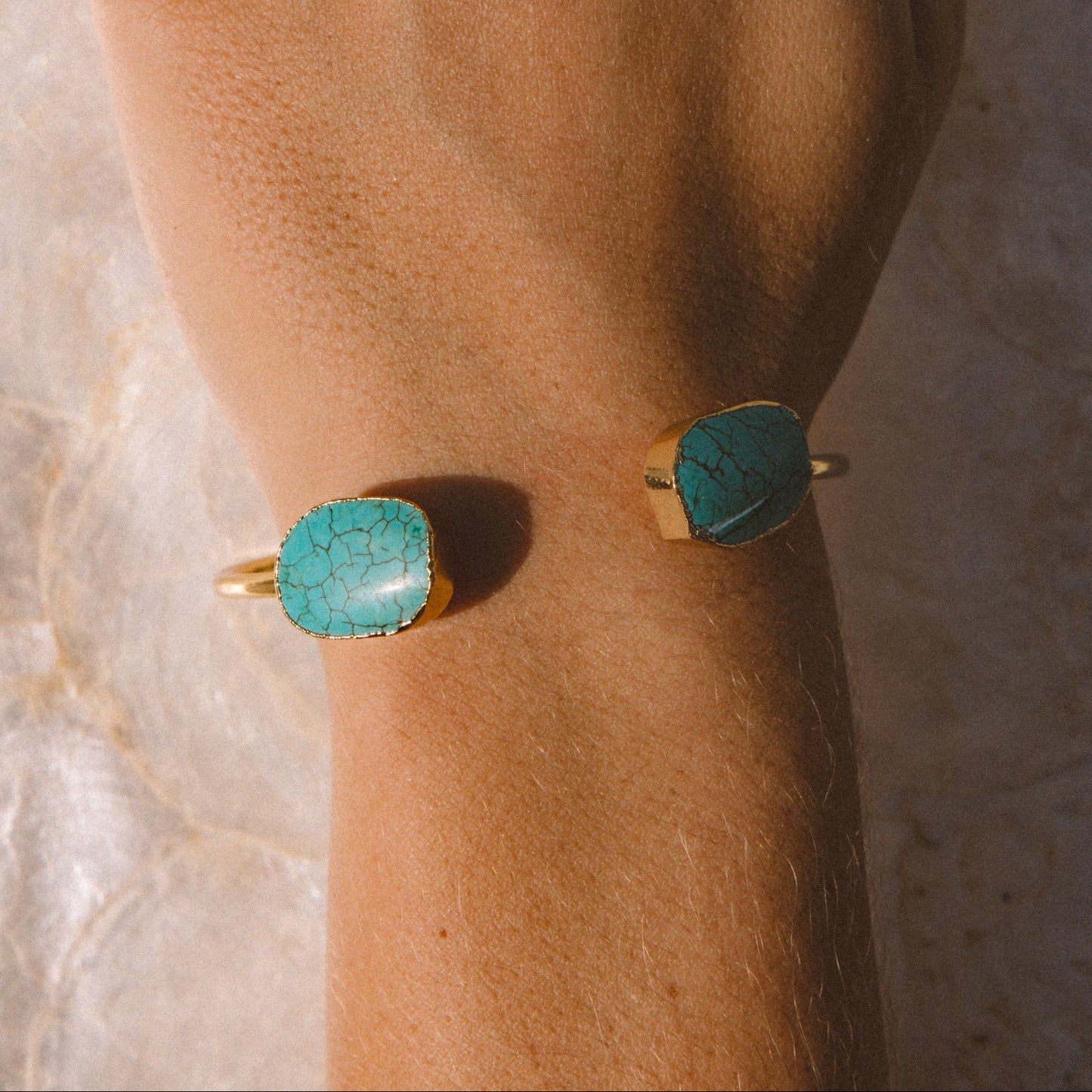 A close-up of a hand wearing multiple rings and two bracelets. The jewelry includes a gold starfish ring with clear stones, a gold ring with a white stone, a gold bracelet with a turquoise stone, and a matching gold bracelet with a rectangular turquoise stone.