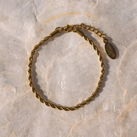 A twisted rope-style gold bracelet with a lobster clasp and extension chain, displayed on a light beige stone surface.