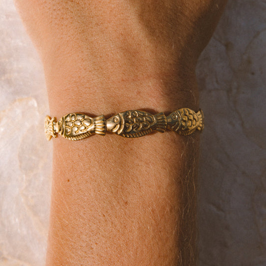 A close-up of a person's wrist wearing a textured gold bracelet against a light stone background.