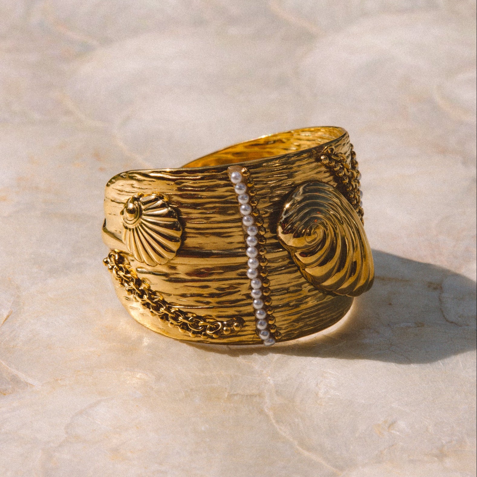 A wide gold ring with textured carvings photographed on a light stone surface.