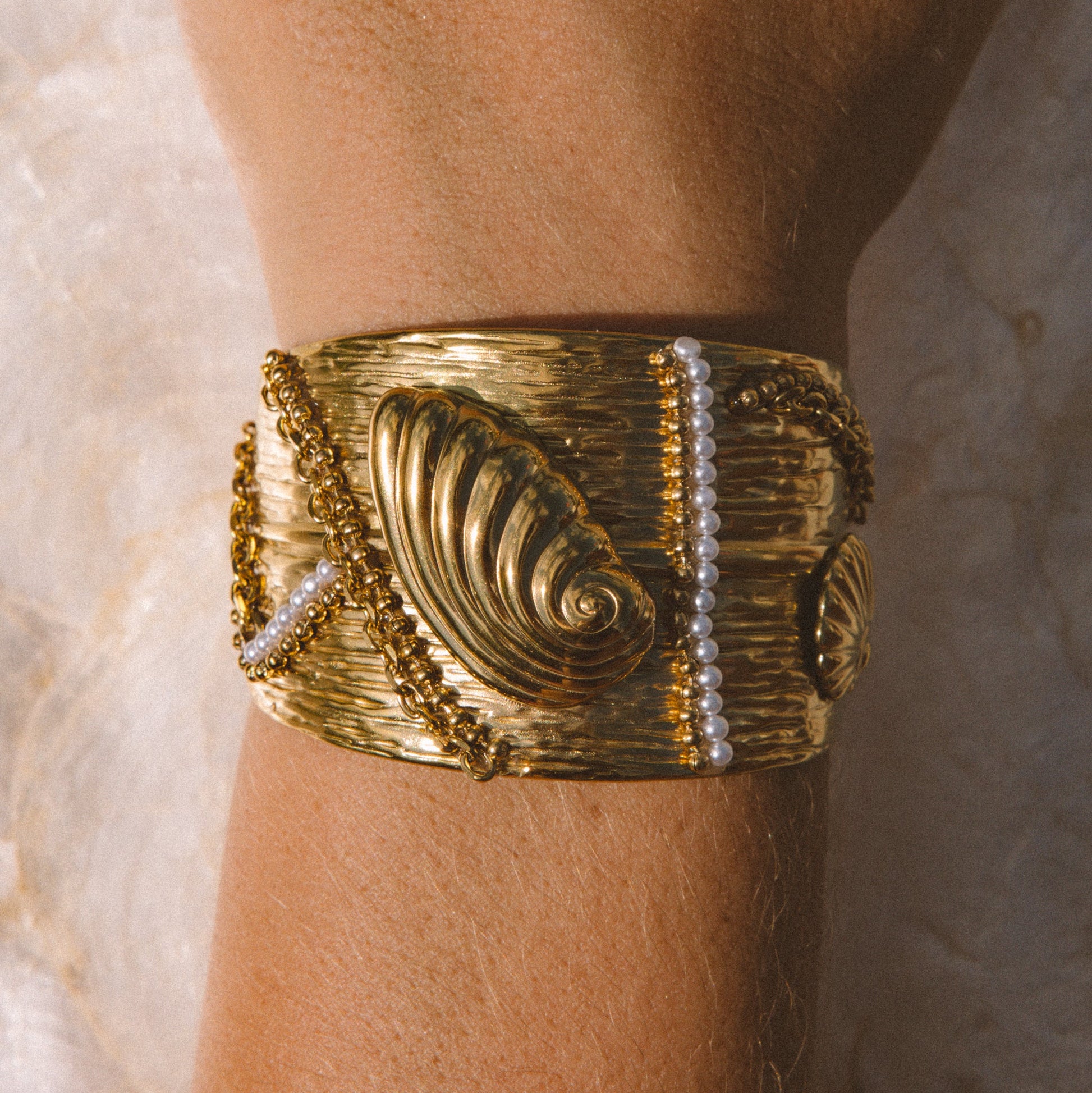 A wide gold cuff bracelet with textured spiral motif and bead details, worn on a person's wrist against a light background.