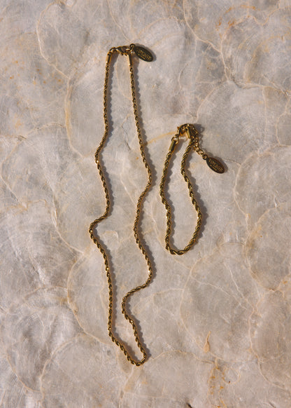A vintage gold-toned chain necklace with a small oval pendant, displayed on a textured beige marble surface.