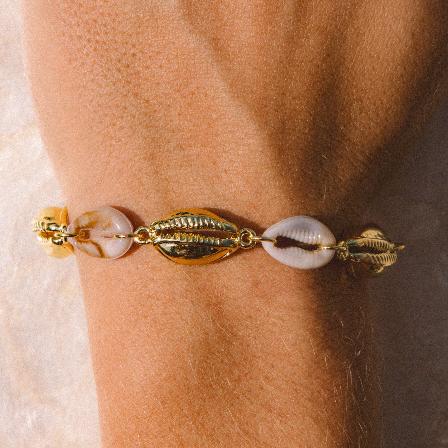 A close-up of a gold-toned bracelet with cowrie shells worn on a person's wrist.