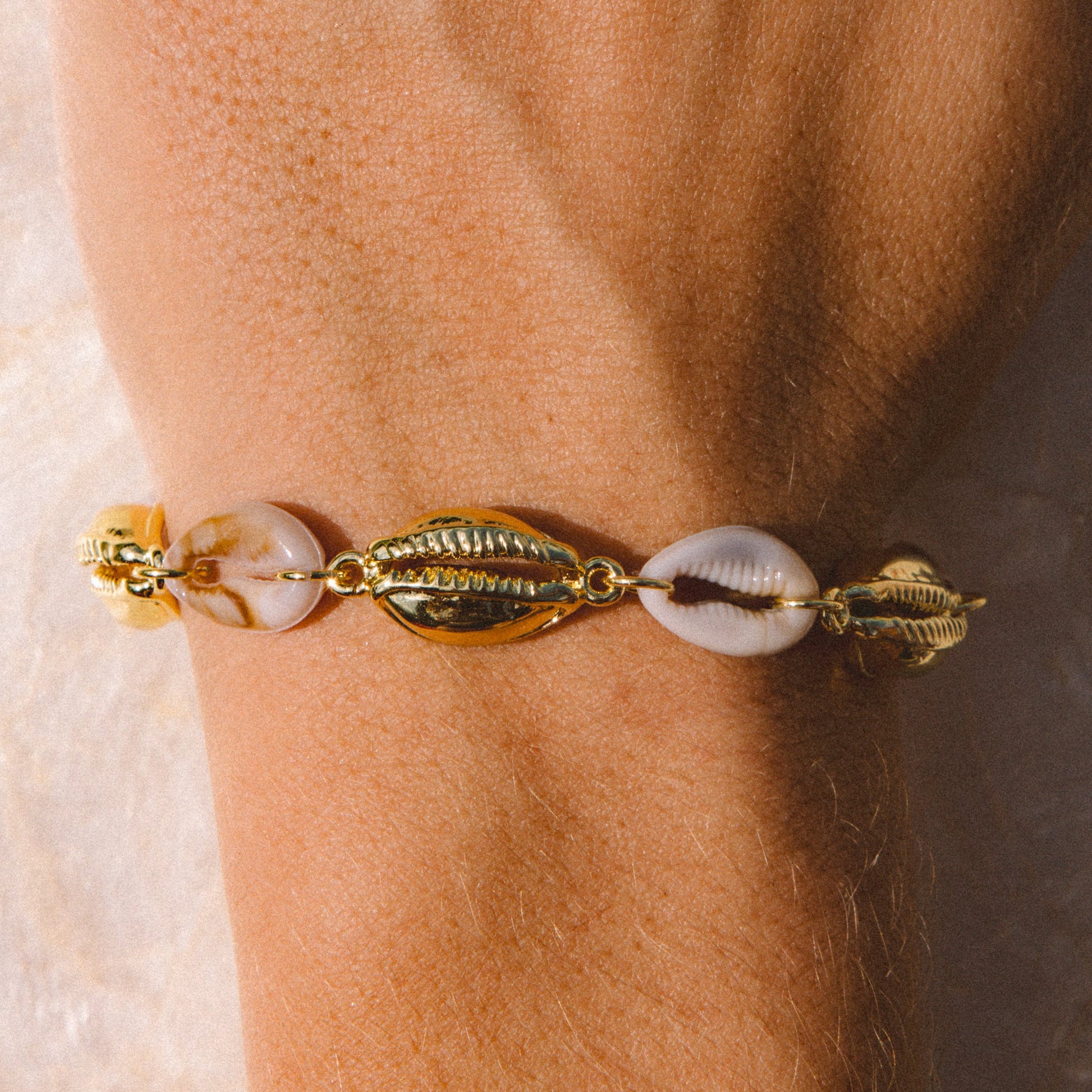A close-up of a gold-toned bracelet with cowrie shells worn on a person's wrist.