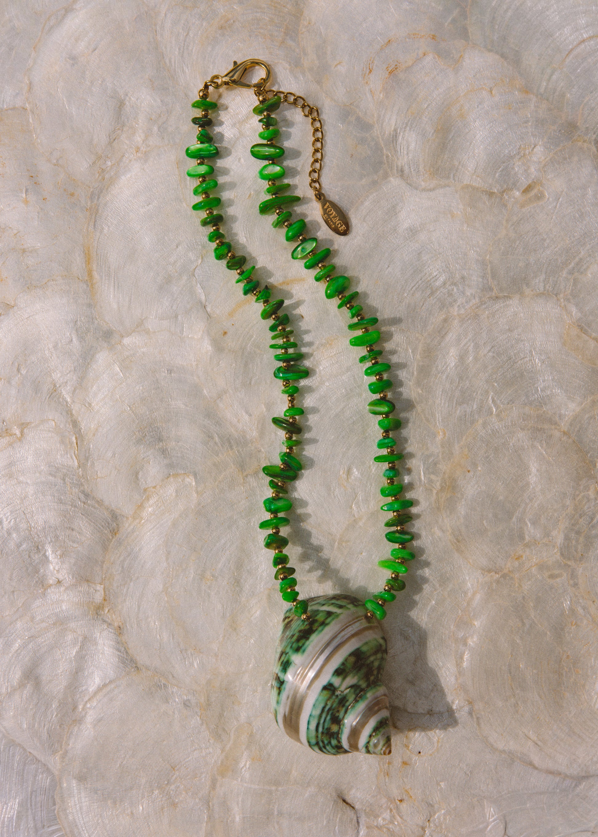 A green beaded necklace with a large green and white striped seashell pendant, displayed on a textured white surface.