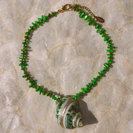 A beaded necklace featuring vibrant green faceted beads and a large green-and-white striped seashell pendant, displayed on a textured white background.