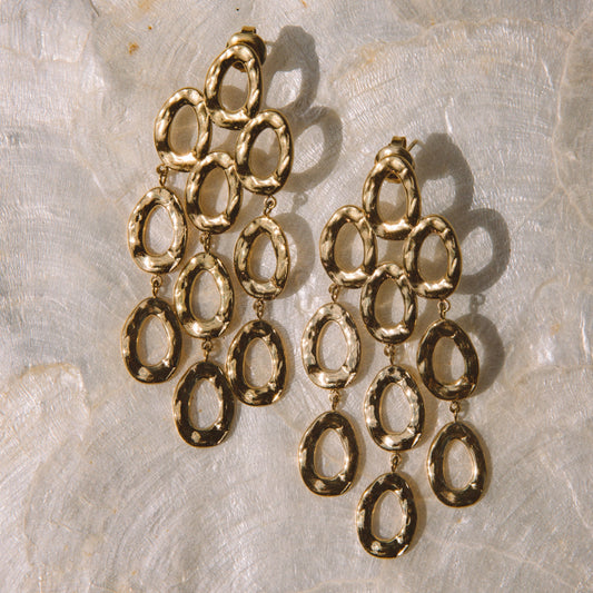 A pair of gold-toned drop earrings with textured oval links, displayed on a textured white surface.