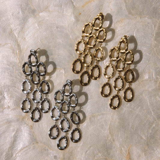 Three pairs of dangling hoop earrings with textured metal links, shown in silver and gold finishes on a light beige marbled surface.