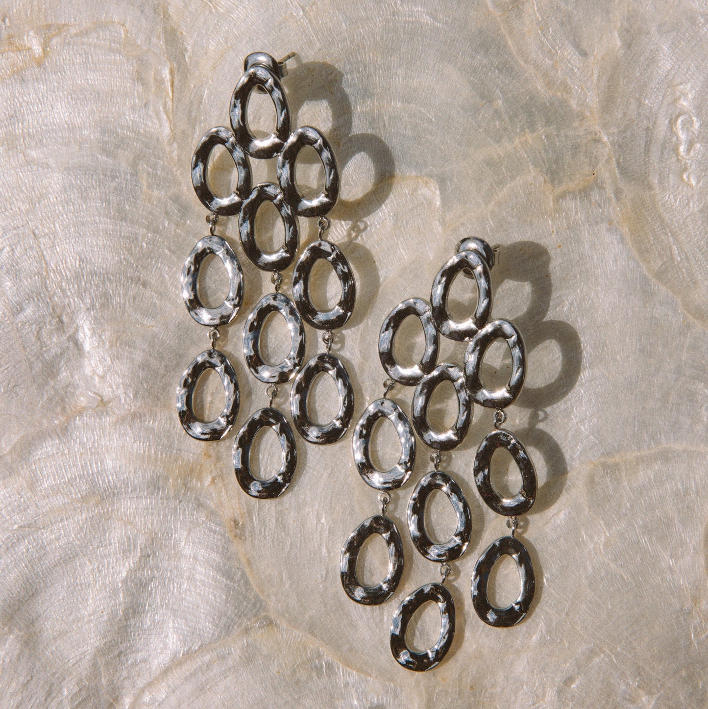 A pair of silver-toned dangling earrings made of multiple linked oval hoops, arranged on a light beige marbled surface.