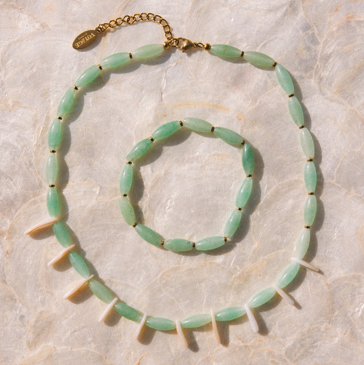 A light green beaded necklace and matching bracelet with gold-tone hardware, arranged on a light beige marble surface.