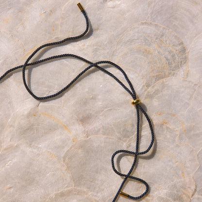 A navy blue cord necklace with small gold metal beads, laid out on a light beige marble surface.
